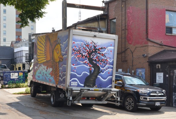 truck with street art painted on it, a tree with pink blossoms on the back and a bird with large wings on the side 