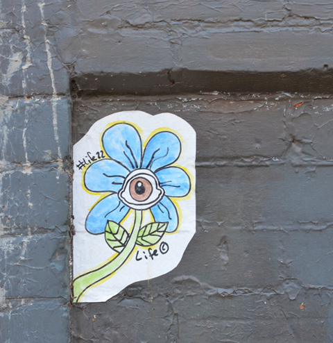 graffiti sticker on a black brick wall, a little blue daisy