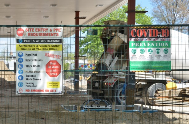 Coid prevention signs secured to a metal fence surrounding a construction site, a cement truck is working there