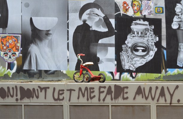 red trike at paste platz, wheatpaste papers on a wall, with words Don't let me fade away 