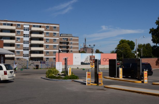 Mcdonalds drive thru lanes with a black car, in front of two apartment buildings now empty and getting ready to be demolished
