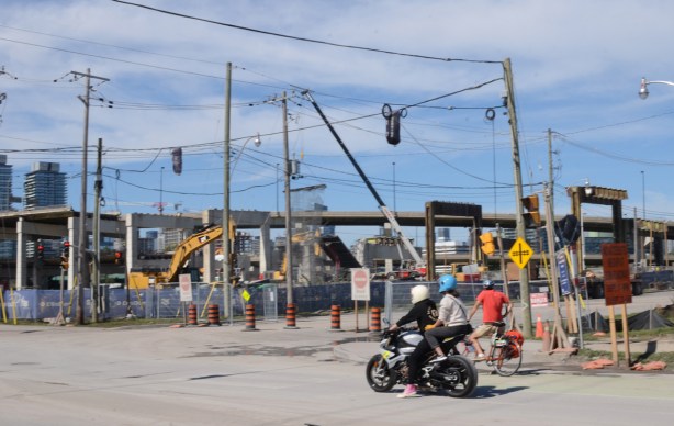 motorcyclists wait for traffic light at intersection of Don Roadway and Villers, construction behind them, removal of eastern portion of the Gardiner Expressway 