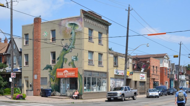 northeast corner of College and St. Clarens, three storey beige brick building with coin laundry on ground floor, large beanstalk mural up the side of the building
