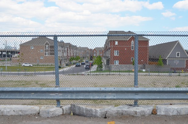 rowhouses on a side street running perpendicular to Kennedy Road, vacant lot in the foreground,