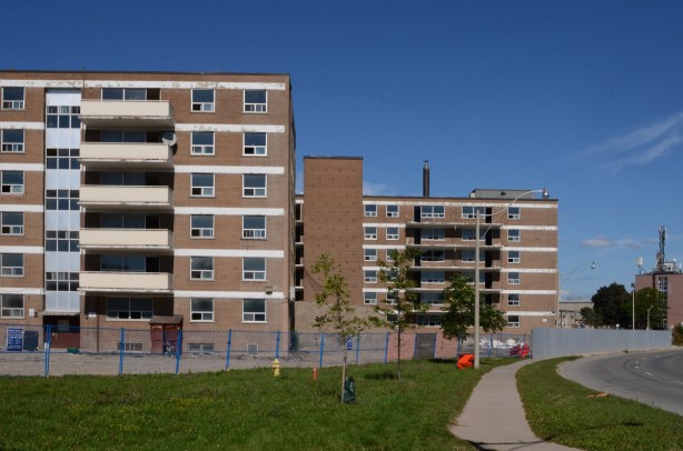 sidewalk along Eastern Avenue, green grassy boulevard, empty apartment buildings behind chainlink fence 