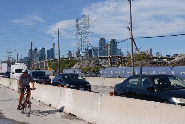 construction zone along Villiers Street, concrete barricades separating car traffic from cyclists, blue fence around construction, demolition of the Gardiner Expressway, skyline in background 