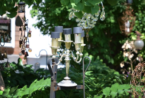a silver candlabra with 5 lights, in a front yard with many other antique light fixtures. 