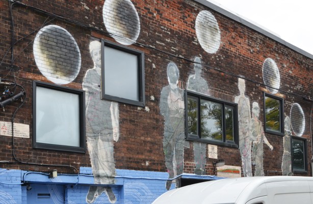 wheatpaste street art installation bymonicaonthemoon on the back of the broadview hotel, 6 large figures black and white photos printed on pieces of old map of the Don River Valley