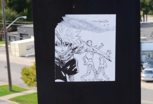 black and white drawing pasteup graffiti on a black metal railing of a bridge