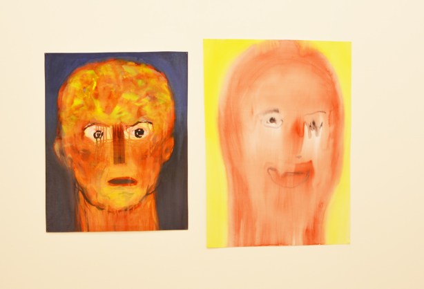 two paintings of faces on a gallery wall 