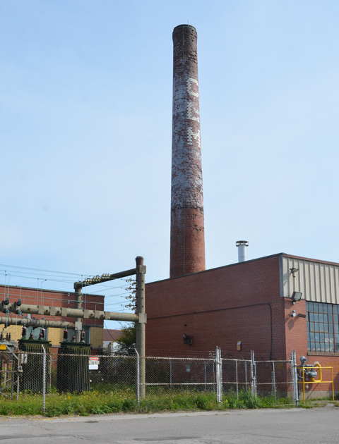 brick chimney with CLM painted on it, beside other industrial buildings