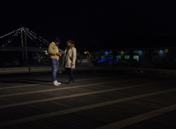a couple, at night, standing outside on one of the wave decks on Queens Quay