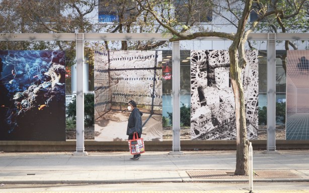 a woman in a mask walks past photo exhibit Future Perfect by Nico Krebs and Taiyo Onorato 