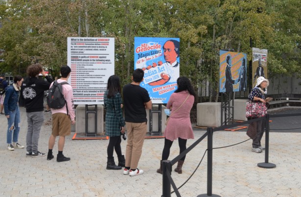 people looking at large posters, part of art installation, built on genocide