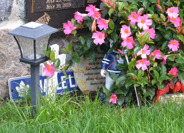 objects left by a tombstone, Maple Leafs sign, and their bear mascot figurine about 8 inches high, pink flowers, and a small white cross with words on it