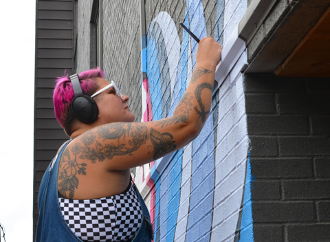 artist, Mo Thuner, on a ladder painting details on a mural with a small paint brush