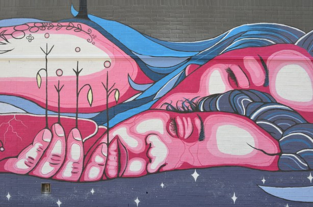 part of a mural by Mo Thunder on Broadview Ave of a mother and child lying in water, child has plants in her hand, mother earth theme, water theme 