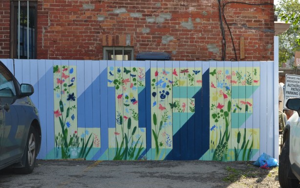 the word life painted on a fence white letters on blue background with small flowers painted all over it. 