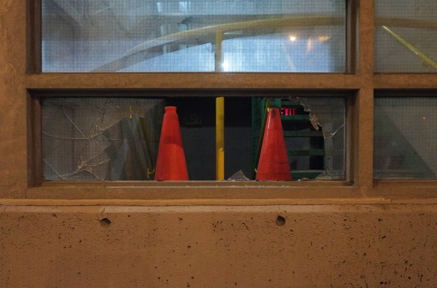 2 small plastic orange pylons sit on a ledge in a broken window with a green staircase behind inside the building