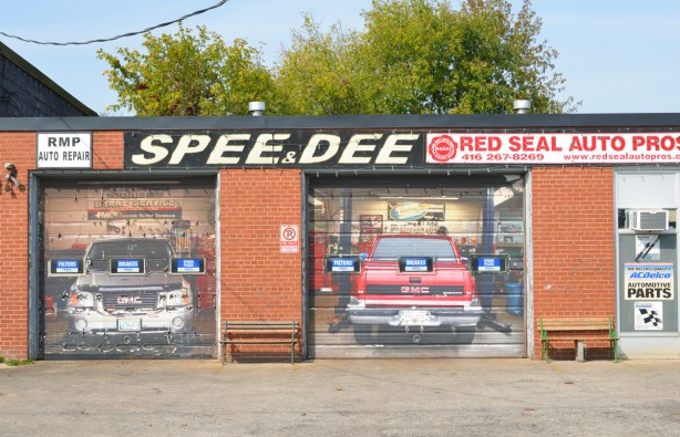 exterior of Spee and Dee Auto Service with garage doors covered with photos of cars in the interior of the garage