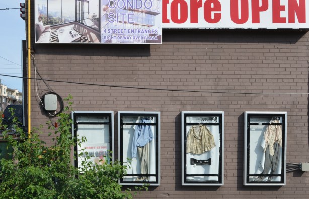 side of empty building with condo sales advert, also four display cases with clothes that are no longer held up properly