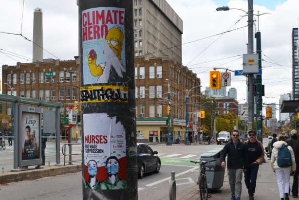 two posters on a metal pole, top one has Homer Simpson