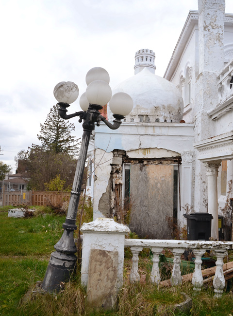 lamp post with 5 globe lights, leaning, outside old white house with multiple architectural styles 