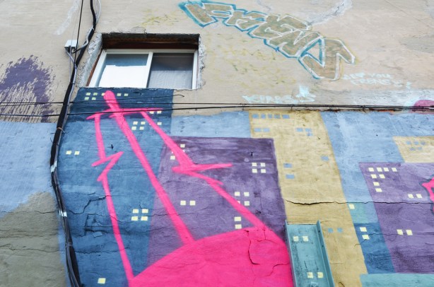 upper part of a mural, city at night with tall buildings and lit windows, pink blob