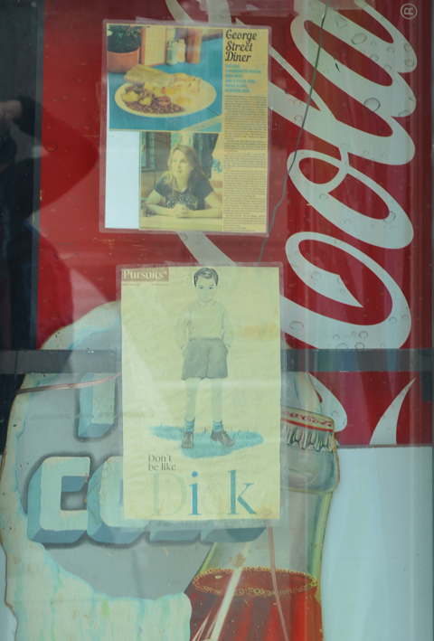 old newspaper articles taped to window with coke machine behind it