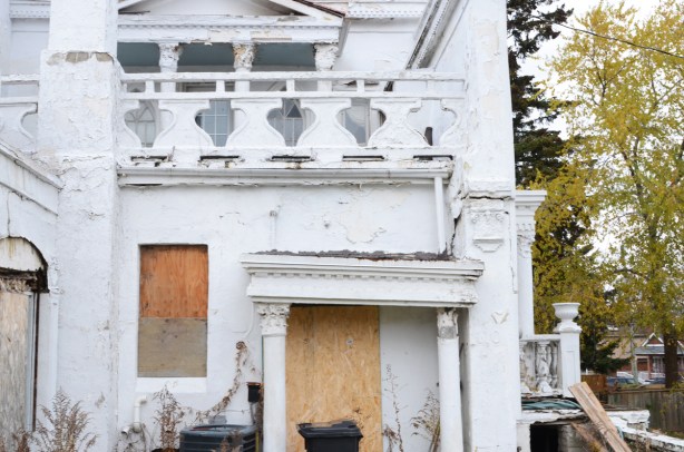 boarded up window and door on old house, railing around balcony above door has heart shaped openings