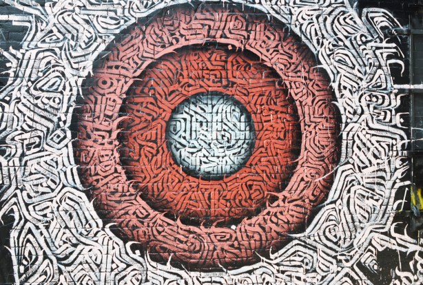 street art by kreecha circles of ornate calligraphy, white in the center, then a red ring, then a pink ring, surrounded by white on black