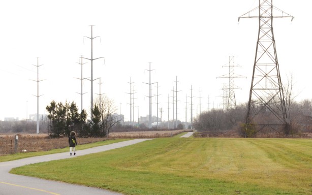 a woman walks on the path through the meadoway with transmission towers and hydro lines, November, 