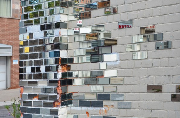an exterior brick wall with some of the bricks covered with rectangular pieces of mirror