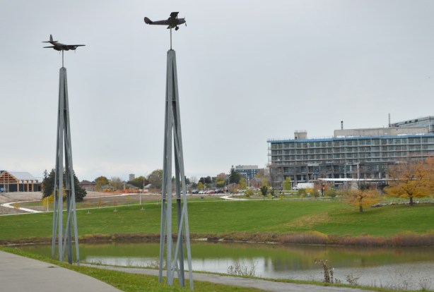 two model airplanes on pillars, look like they are flying above a pond, park, and new apartments under construction 