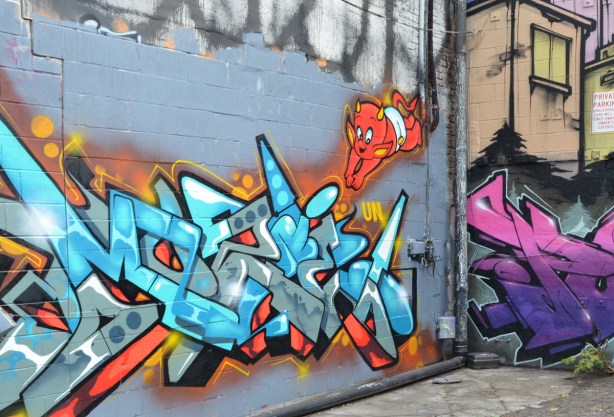 street art in El Mocambo Lane, grit laneway, blue text tag with little orange devil diving into it. devil wearing only a white diaper