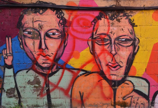 part of a mural, two men with short hair, one has his arm around the shoulder of the other, head and shoulders view 