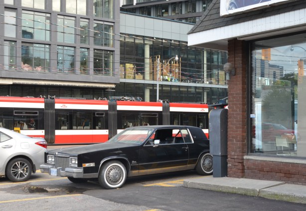 an old car from the 70s parked beside a building, a new TTC streetcar behind