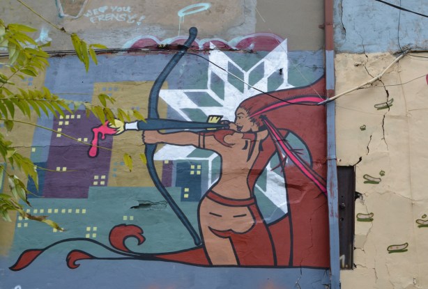 female archer with arrow as a paint brush dripping with pink paint, street art in a toronto lane