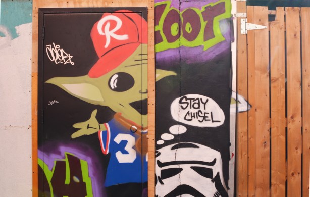 a little green yoda like figure with a red baseball cap, peering out from behind a door