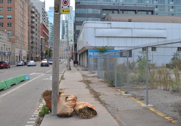 bags of yard waste lie on the sidewalk on Richmond Street on sidewalk by large vacant lot, east of Sherbourne