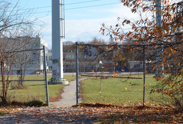 gap in chainlink fence under hydro transmission lines, with path leading to a school 