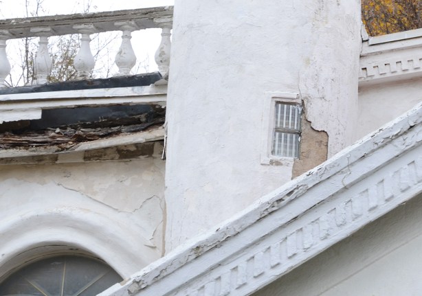 small window in a crumbling building, plaster coming off wall, wood deteriorating along roofline