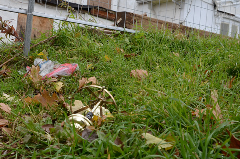 brass remnants from something lying in the grass with dead leaves outside an empty and abandoned house