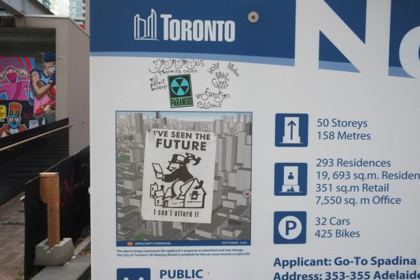 blue and white city of toronto notice of development sign, on which someone has put a sticker with Mr. Monopoly and the words I have seen the future and I can't afford it 
