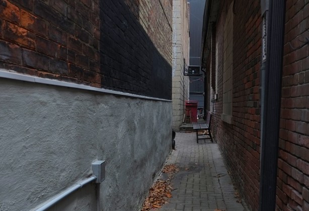 very narrow passageway between two red brick buildings with a bench at the end
