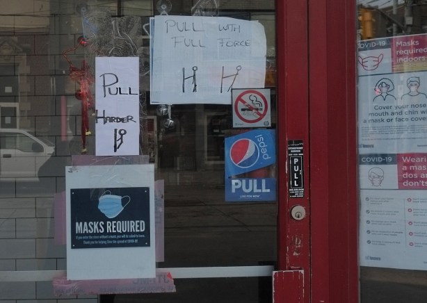 signs on a restaurant door that say pull with all your force and another sign that says pull harder. also covid signs like masks required and public health posters