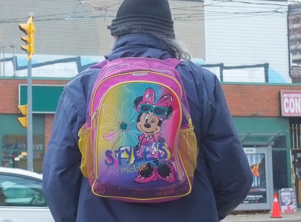 an elderly man with long gray hair wearing a backpack with Minnie Mouse and words that say style is my middle name