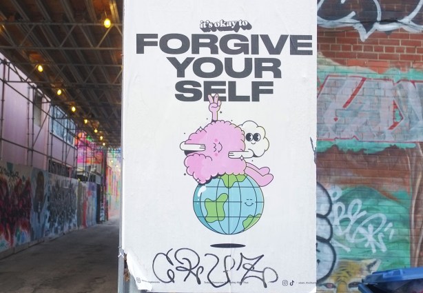 poster graffiti that says It's okay to forgive yourself, a white cloud is giving a pink blob a big hug and they are both sitting on top of a globe of the earth