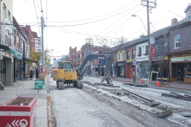 a yellow digger is the middle of Queen Street West removing street car tracks, west of Euclid
