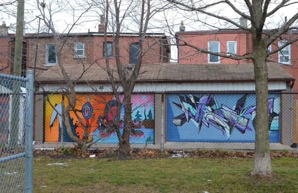 looking across a park in late December, two garages in an alley painted with murals, on the right is one in blues by mediah 
